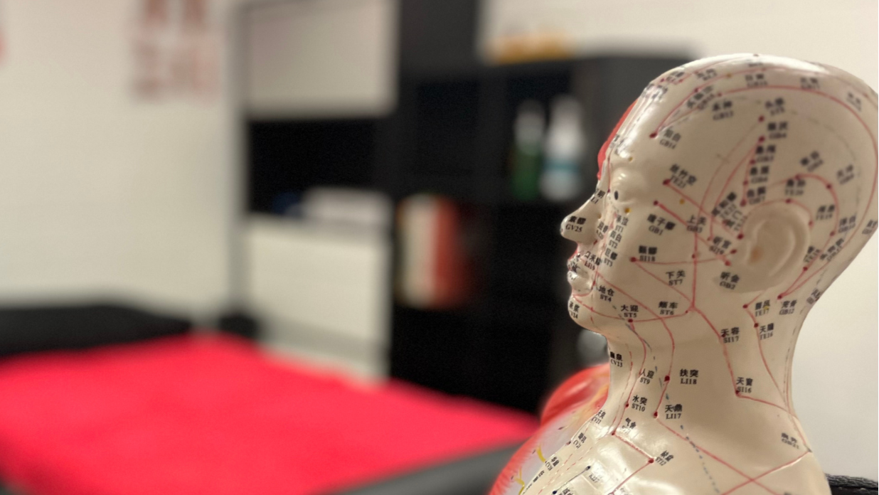 Acupuncture model with text about traditional methods for modern problems in a blurred therapy room setting.